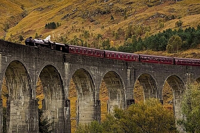 Maroon carriages crossing tall concrete arches below a brown autumn hillside