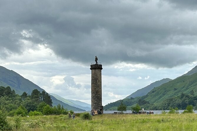 A tall stone column with a figure on top, hills closing in behind